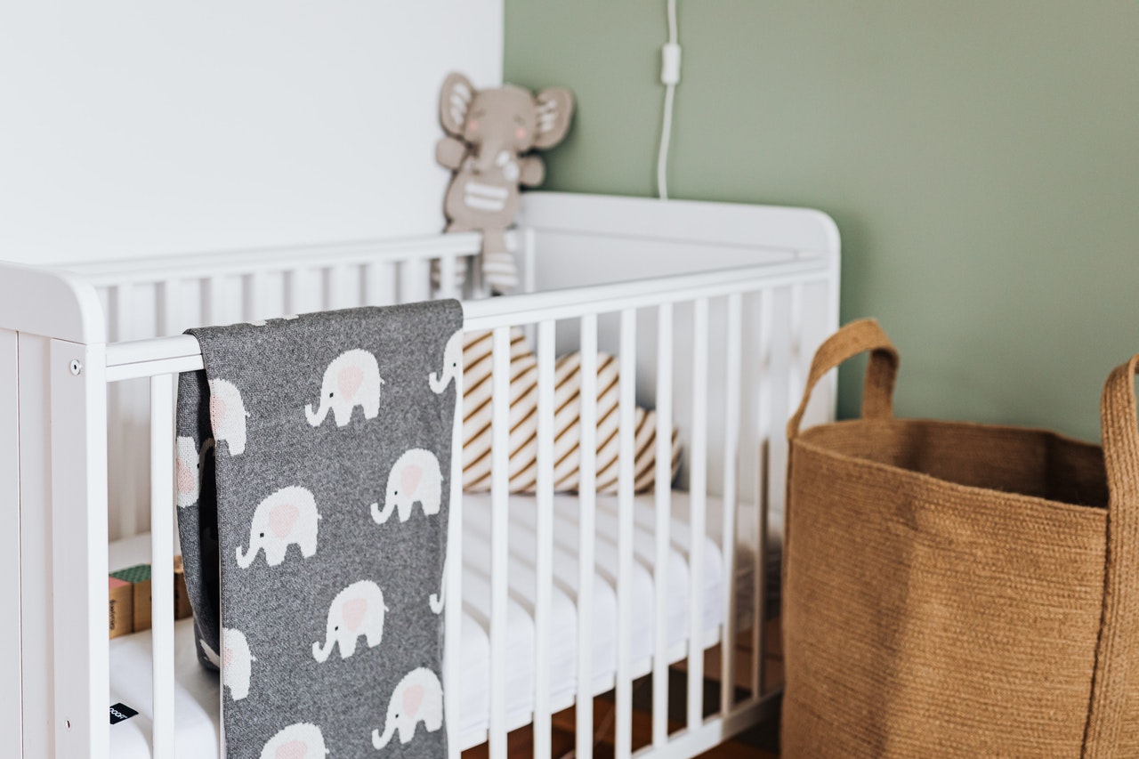 Grey baby swaddle hanging over a white baby cot