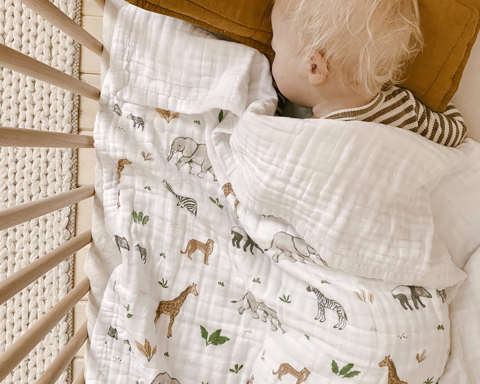 Baby sleeping in a wooden cot with an organic cotton patterened blanket