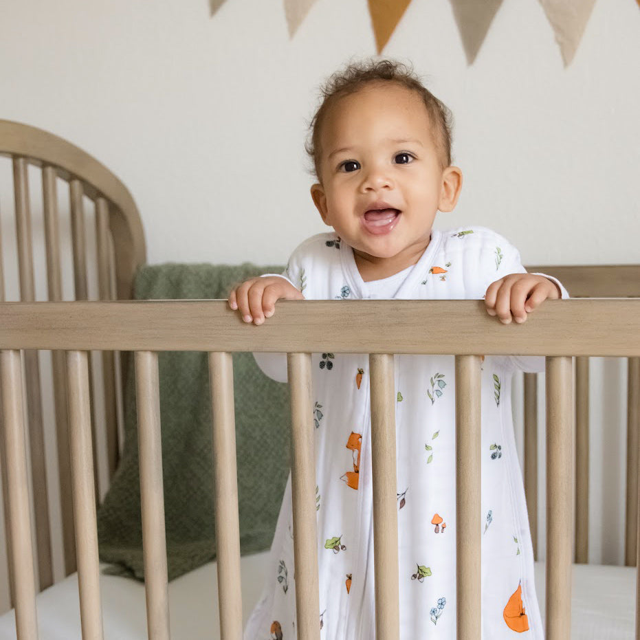 Organic baby sleeping back collection - baby standing up in a wooden cot