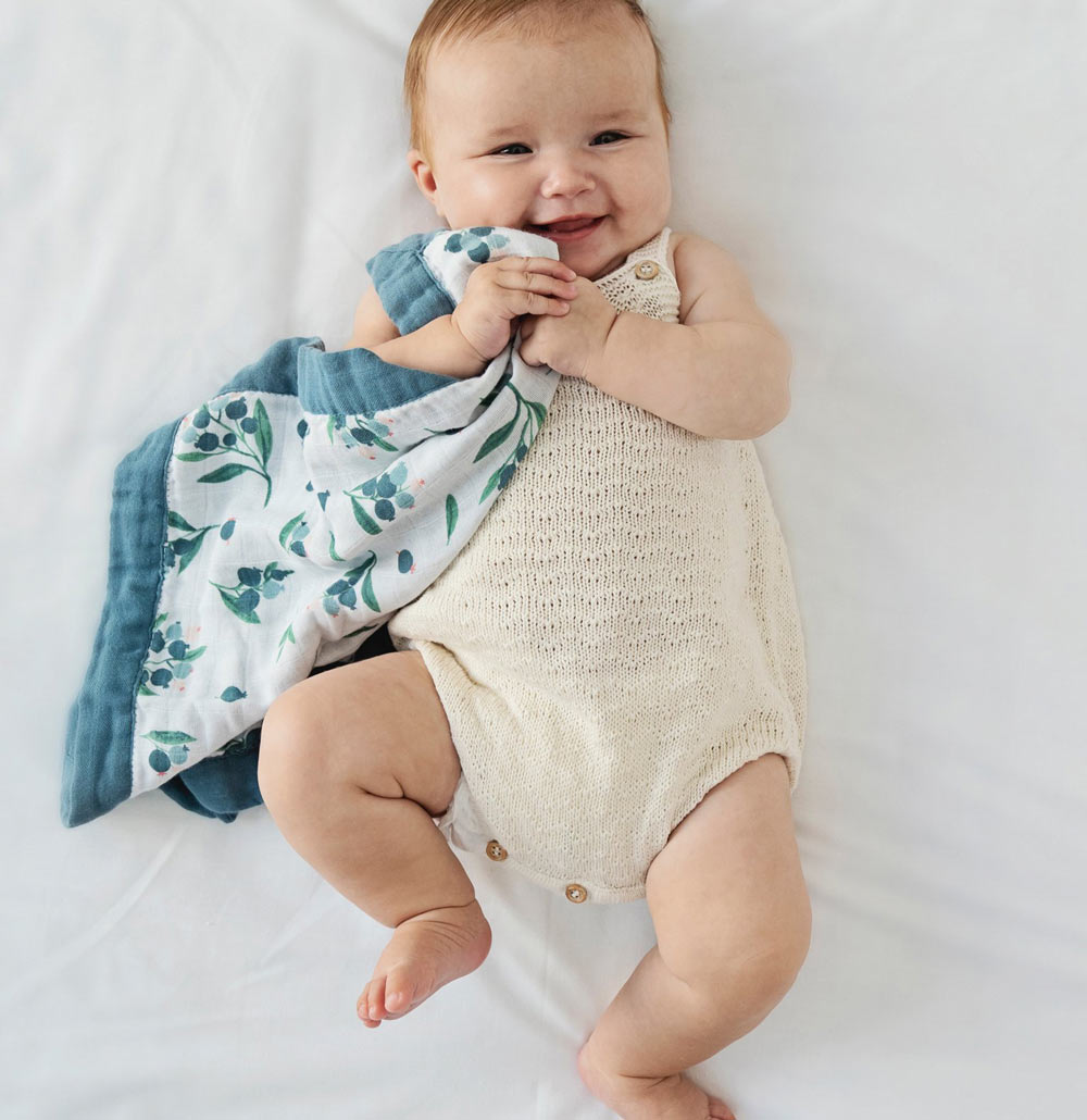 Laughing baby clutching a cotton muslin comforter