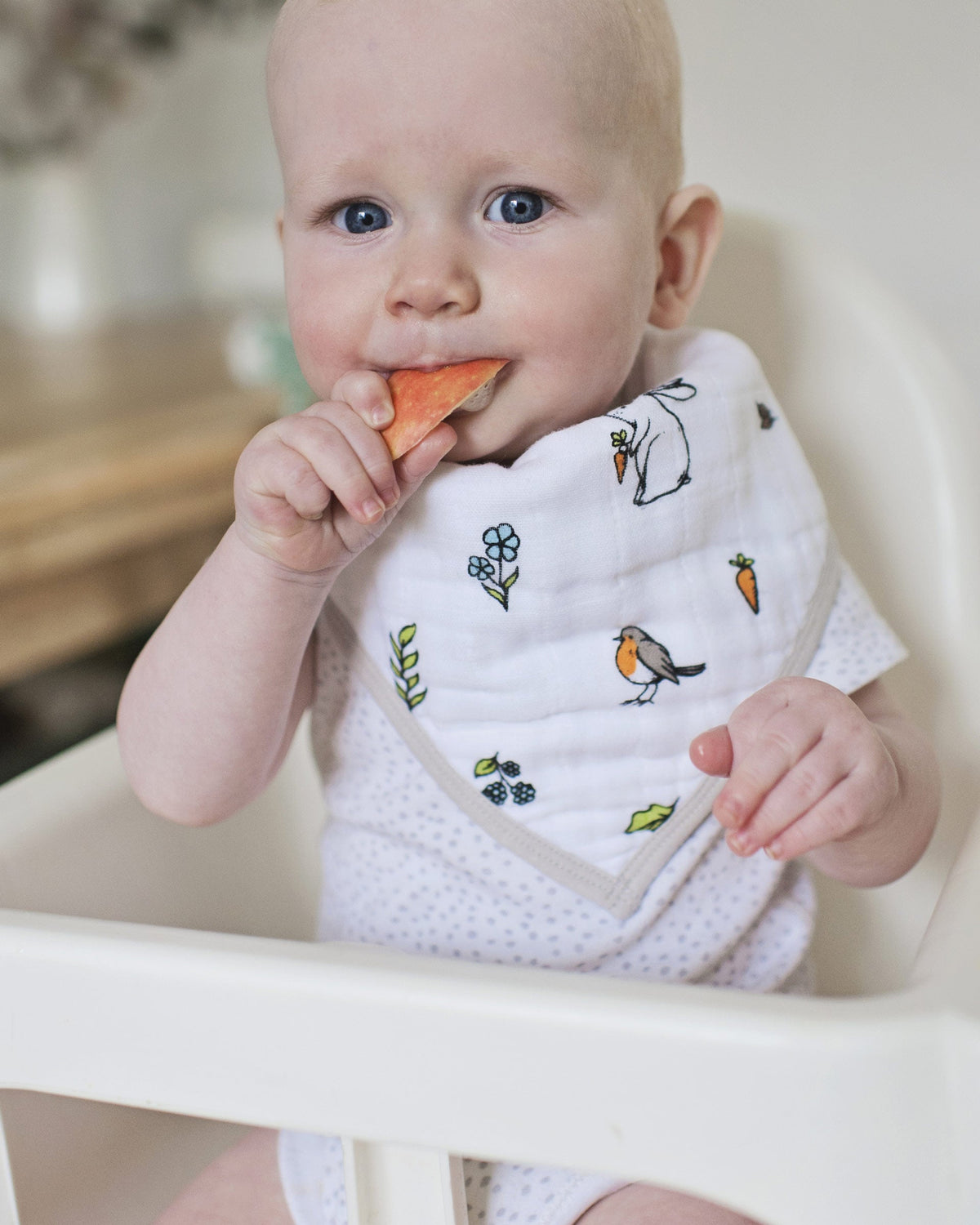 Adjustable organic baby bandana bib with woodland pattern worn by baby eating an apple